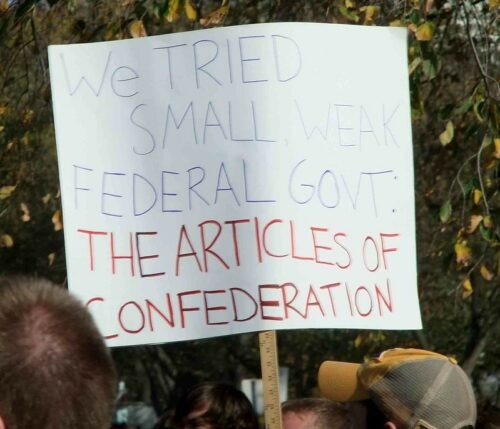 A handwritten protester's sign reads "We tried small, weak federal govt: the articles of confederation" in all caps.