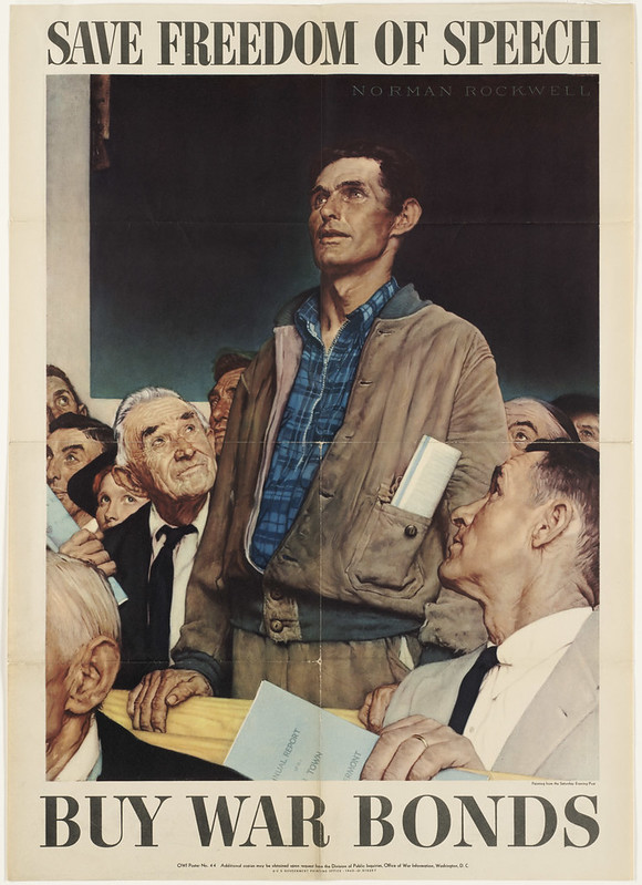 A blue collar working man stands amidst a crowd of men in white collar suits, looking up as if addressing someone.