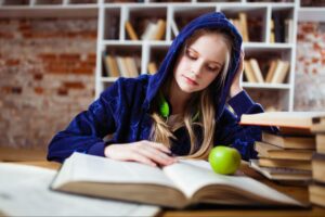 Photo of a girl in a blue sweatshirt reading a book in a library