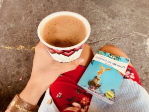 A photo of someone holding a cup of coffee with their left hand and a Ciudad de México guidebook on her lap. 