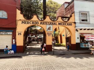 A photo from across the street of a beige double archway, with "Mercado artesanal mexicano" across the top