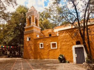 A photo of an orange stucco building with a bell tower on one end.