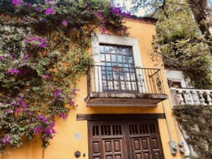 A photo of an orange stucco house with a balcony and flowering vines growing up the wall.