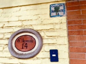 An address sign on the outside of a cream brick building, labeled "C. Aguacate 14" 