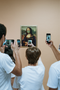 Photo of people taking pictures on their phones of the Mona Lisa, who is wearing a mask.