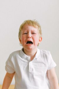 Photo of a white blonde-haired boy in a white polo shirt crying.