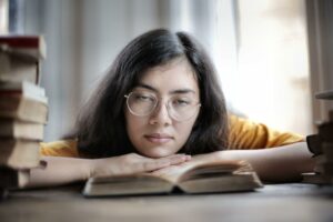 Photo of a girl with glass resting her chin on an open book