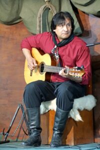 A gaucho sitting and playing a guitar in front of a microphone