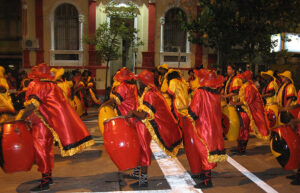 A parade of drummers wearing red and yellow cloaks