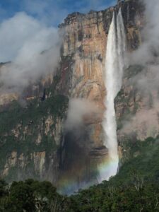 A tall waterfall falling down a cliff, with a rainbow forming in the mist at the bottom