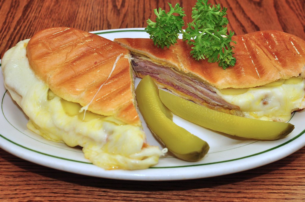 A melty cheesy Cuban sandwich on a plate with pickles