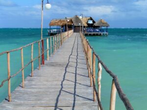 A wooden bridge out to a pier above turquoise ocean