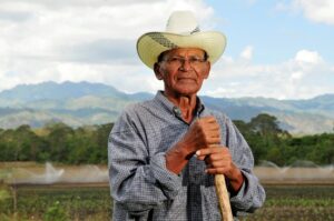 A photo of a Nicaragauan farmer in front of his farm, wearing a hat.
