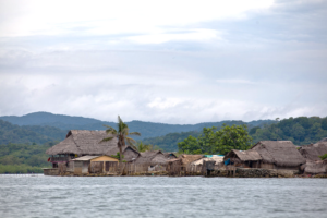 Thatch huts near the water, with mountains in the background.
