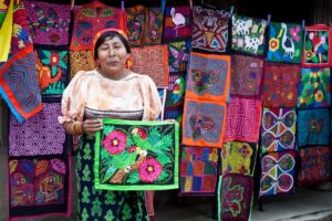 A woman with mola displayed behind her shows off a piece.