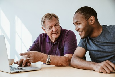 An older white man and a younger black man look at a computer together