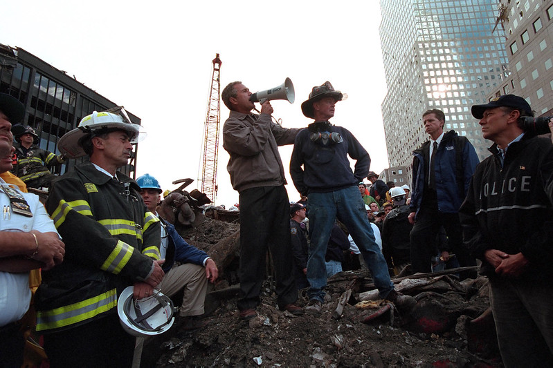 Original caption: Standing atop rubble with retired New York City firefighter Bob Beckwith, President George W. Bush rallies firefighters and rescue workers during an impromptu speech at the site of the collapsed World Trade Center in New York City.