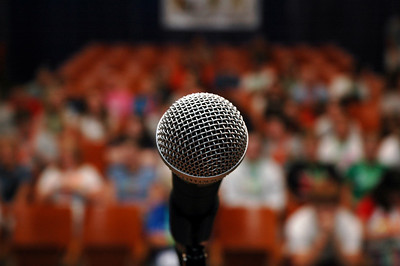 Close-up photograph of a microphone with a blurry audience in the background