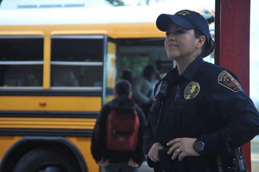 Security officer stands while kids step onto a school bus