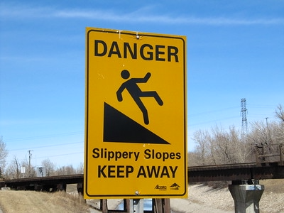 A yellow street sign with a falling person that says, "Danger. Slippery Slopes. Keep Away"