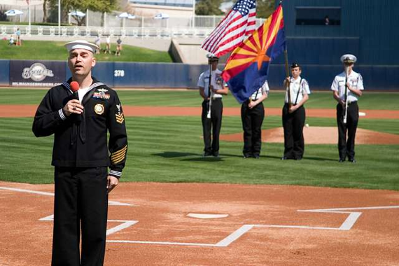 A man dressed in a Navy uniform sings on a baseball field