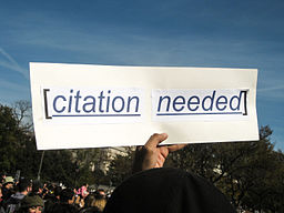 Hand holding a sign that reads, "Citation needed"