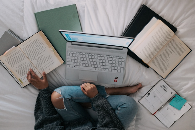 Woman sitting on bed in front of an open computer and open books